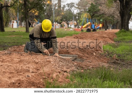 Construction worker with hard hat checking ground level using spirit level and straightedge in public park