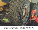 A construction worker in a hard hat examines the massive tire of a heavy machinery vehicle, ensuring it is in good condition while on the job.