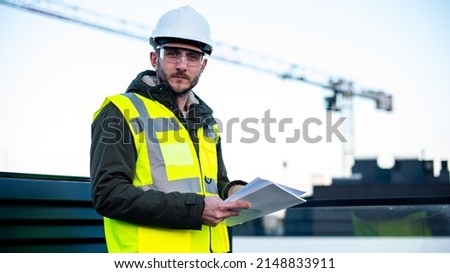 A construction worker in a hard hat helmet protect glasses looks forward at camera and smiles because of sustainability of industry. Concept of construction engineering works and real estate. 
