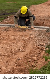 Construction worker with hard hat leveling concrete base using aluminum straightedge and spirit level