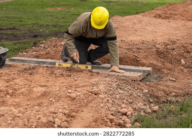 Construction worker with hard hat leveling concrete base using aluminum straightedge and spirit level