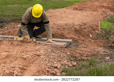 Construction worker with hard hat leveling concrete base using aluminum straightedge and spirit level
