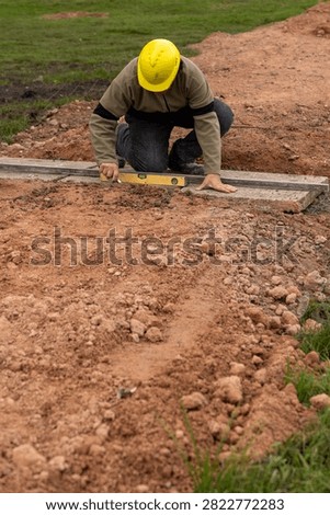 Construction worker with hard hat leveling concrete base using aluminum straightedge and spirit level