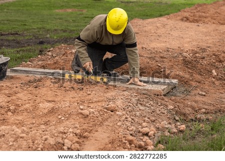 Construction worker with hard hat leveling concrete base using aluminum straightedge and spirit level