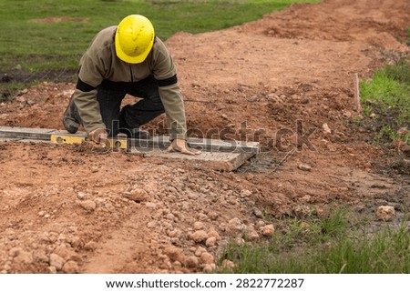 Construction worker with hard hat leveling concrete base using aluminum straightedge and spirit level
