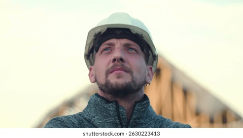 Construction worker in hard hat looking upward confidently, open structure in background, symbolizing vision, pride, and commitment to construction excellence