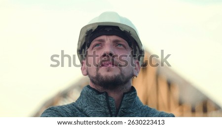 Construction worker in hard hat looking upward confidently, open structure in background, symbolizing vision, pride, and commitment to construction excellence