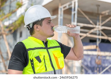 Construction worker in a hard hat and safety vest drinking water, staying hydrated during work on a building site. - Powered by Shutterstock