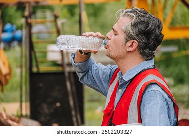 Construction worker in a hard hat and safety vest drinking water, staying hydrated during work on a building site. - Powered by Shutterstock