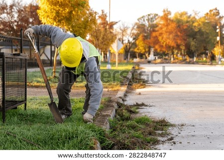 Construction worker with hard hat and safety vest edging lawn with spade shovel along street curb