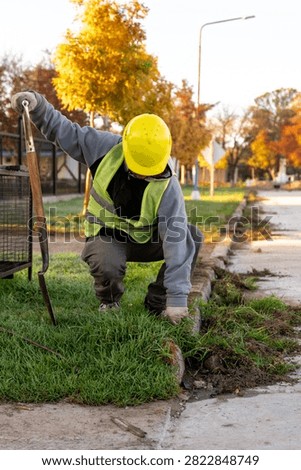 Construction worker with hard hat and safety vest edging lawn with spade shovel along street curb