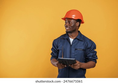 Construction worker in hard hat and with tablet. Handsome black man is in the studio against yellow background.