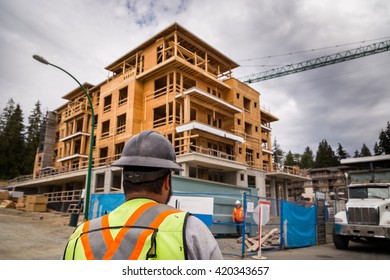 Construction Worker In A Hardhat Observes An Apartment Complex Under Construction. 