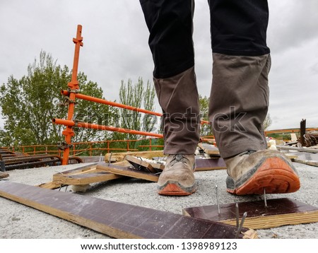 A construction worker has an accident while walks through a site with debris and stepping on a nail 
