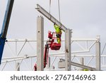 Construction worker in high visibility gear guides steel beam into position on concrete frame