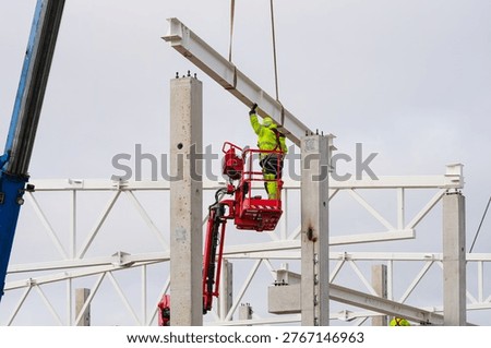 Construction worker in high visibility gear guides steel beam into position on concrete frame