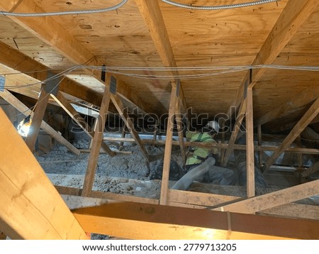 Construction worker installing blown in insulation inside a residential attic crawlspace. Suitable for concepts involving home improvement, energy efficiency, insulation services, construction work, HVAC systems, and residential maintenance.