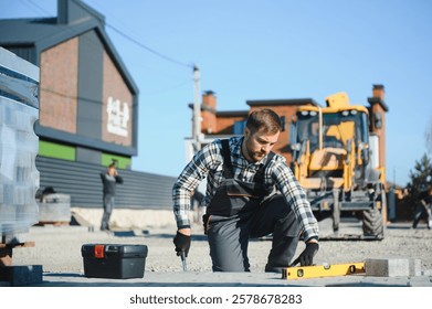 Construction worker installing and laying pavement stones on terrace, road or sidewalk. Worker using stones and rubber hammer to build stone sidewalk.