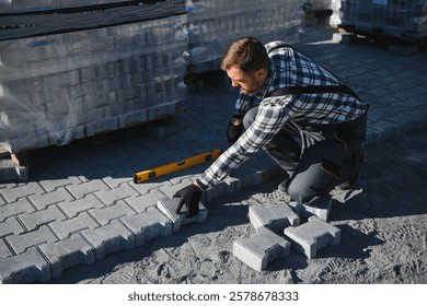 Construction worker installing and laying pavement stones on terrace, road or sidewalk. Worker using stones and rubber hammer to build stone sidewalk.