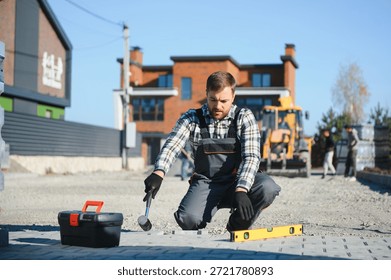 Construction worker installing and laying pavement stones on terrace, road or sidewalk. Worker using stones and rubber hammer to build stone sidewalk.