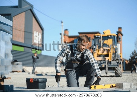 Construction worker installing and laying pavement stones on terrace, road or sidewalk. Worker using stones and rubber hammer to build stone sidewalk.