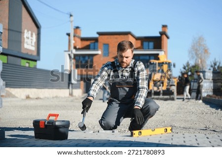 Construction worker installing and laying pavement stones on terrace, road or sidewalk. Worker using stones and rubber hammer to build stone sidewalk.