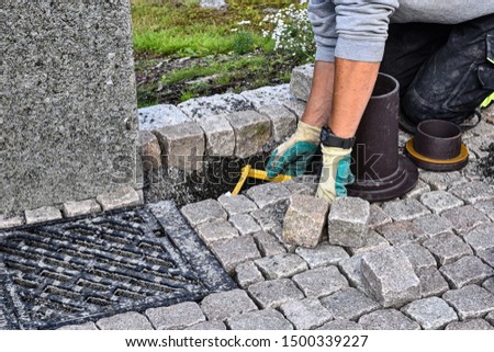 Construction worker installing natural gray stone blocks on pavement in Norway. 