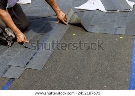 Construction worker installing new bitumen shingles on roof house using air nail gun