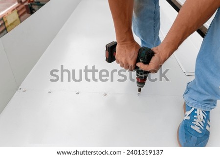 Construction worker installing new metal sheet roof. Man with cordless drill screws the roofing sheet to the roof of a house.