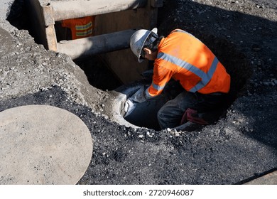 Construction worker installing precast concrete ring to utility hole access point for new public sewer system infrastructure installation project in dug up street
