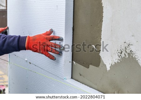 Construction worker installing styrofoam insulation sheets on house facade wall for thermal protection.