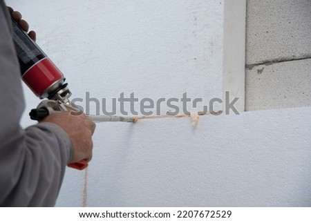 Construction worker installing styrofoam insulation sheets and filling space between with expanding foam on house facade wall for thermal protection. Thermal insulation.