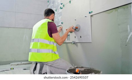 Construction Worker Installing Wall Tiles with Suction Tool. Back view of a construction worker in a safety vest installing large wall tiles using suction tools in a modern interior space.