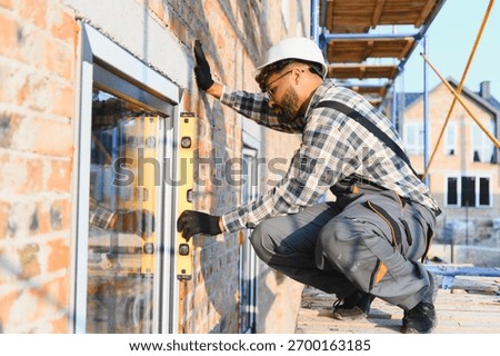 Construction worker installing a window on a brick house facade, using a spirit level for precise alignment. Building new home