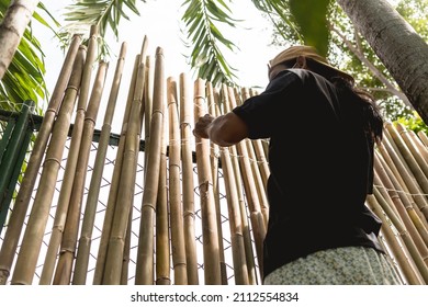A construction worker installs bamboo wall panels tied together with nylon to cover a chain link fence. Home renovation and beautification.