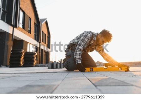 Construction worker kneeling, checking the level of newly laid paving on a modern building site at sunset