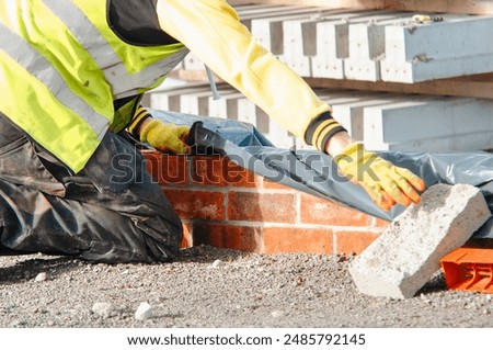 Construction Worker Kneeling While Placing Brick on New Brick Wall