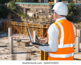 Construction worker with laptop. Man engineer near construction site. Builder with computer with back to camera. Man inspector watching construction process. Erection of skyscraper basement