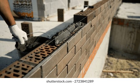 Construction worker laying bricks with mortar, creating a new wall on a building site. Manual labor and new beginnings concept