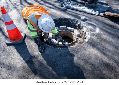 Construction worker laying bricks on top of a sewar access entrance pipe to raise up the level before installing the access collar, road construction project
