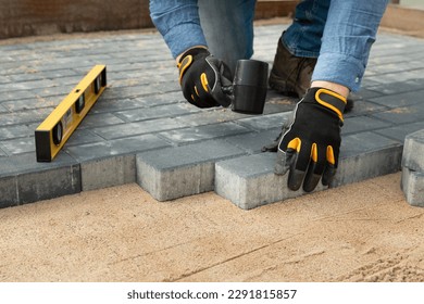 Trabajador de la construcción tendiendo pavimento de cemento en una pasarela con guantes y martillo de goma. Mejora de la vivienda.