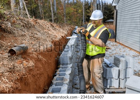 Construction worker of laying drainage pipe for rainwater in during mounting retaining wall.