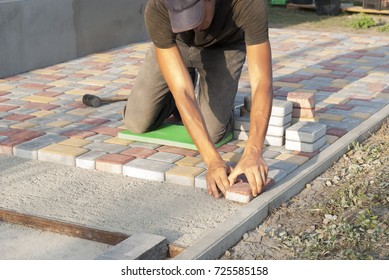 construction worker laying sidewalk tiles in the yard of the house