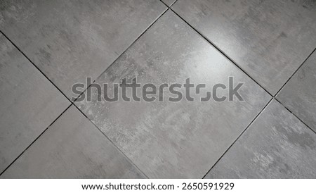 Construction worker laying square gray concrete effect porcelain stoneware tiles on a bathroom floor