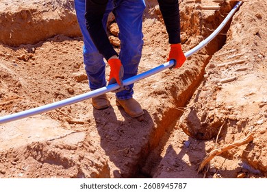 Construction worker lays electrical pipe in filled trench during foundation work