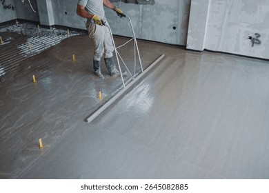 Construction worker leveling concrete surface flooring using smoothing trowel, creating smooth and even finish