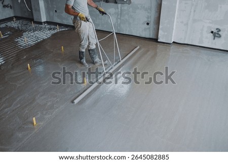 Construction worker leveling concrete surface flooring using smoothing trowel, creating smooth and even finish