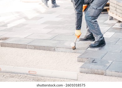 A construction worker leveling pavement tiles with a rubber mallet during roadwork. The process ensures stability and precision in urban infrastructure and landscaping projects.