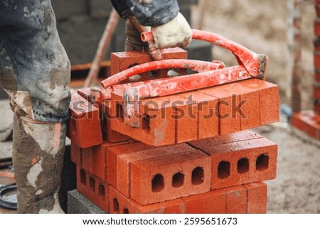 Construction worker lifting red bricks at building site