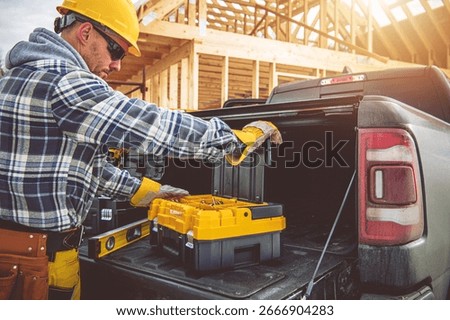 A construction worker lifts toolboxes from the back of a truck at a building site during daylight, preparing for a day of work on the project.